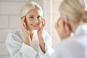 Woman in her late 50s looks at her reflection in the mirror to see rejuvenated eyes